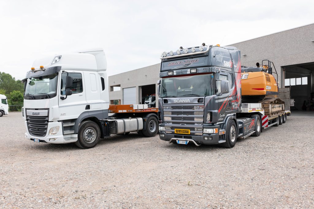 Trattore stradale pianale con rampa DAF accanto a un camion Scania che trasporta un escavatore
