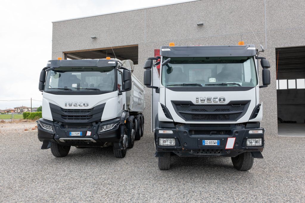 Due autocarri a quattro assi Iveco con cassoni ribaltabili parcheggiati fianco a fianco in un piazzale