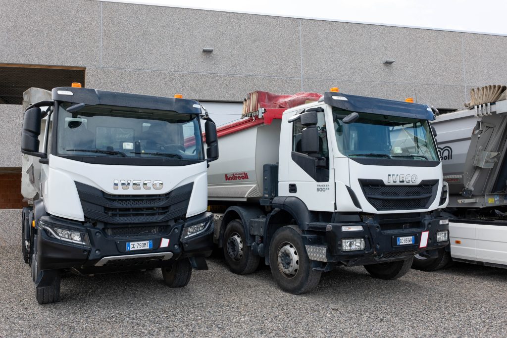 Autocarri quattro assi Iveco con cassoni ribaltabili parcheggiati davanti a un capannone