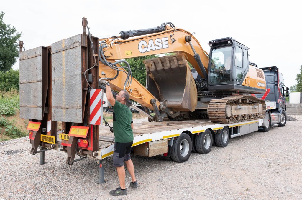 Escavatore CASE caricato su semirimorchio mentre un operatore chiude le rampe di carico