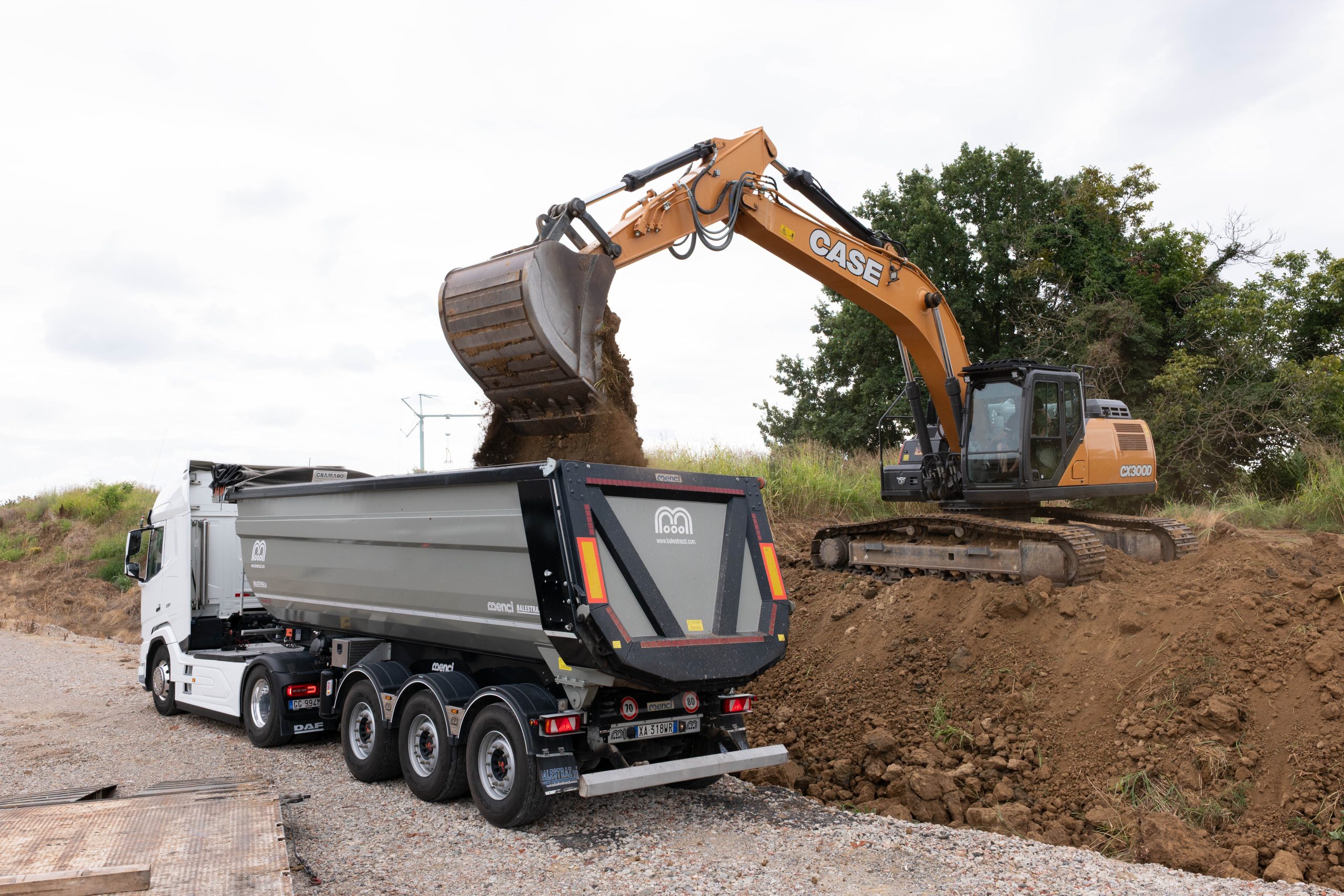 Escavatore CASE che carica terra nel cassone di un camion in cantiere