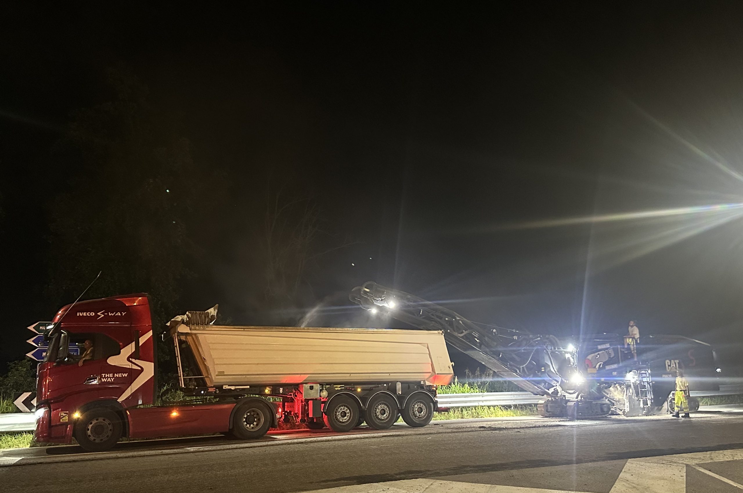 Camion e macchina stradale lavorano di notte su una carreggiata illuminata